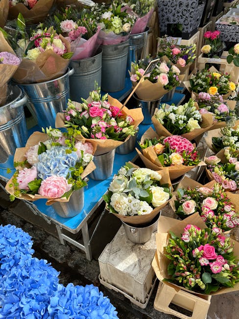 A vibrant display of freshly arranged flower bouquets placed on a table at a floral shop. The arrangements feature a variety of flowers including pink roses, white roses, light blue hydrangeas, and sm